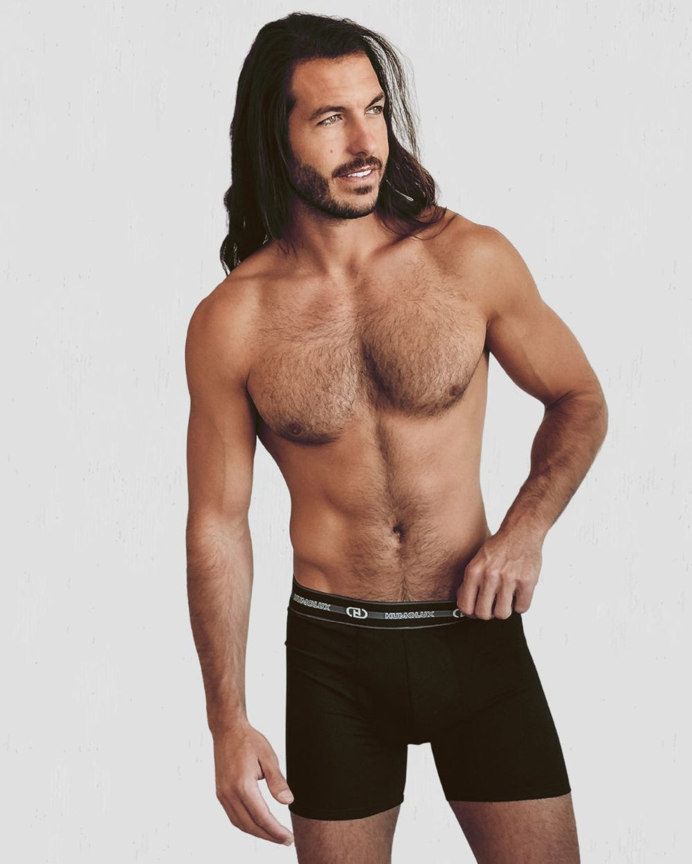A shirtless man with long dark hair models black boxer briefs against a light gray studio background. The waistband has a small white logo with the word 'BICHOFFEN'.
